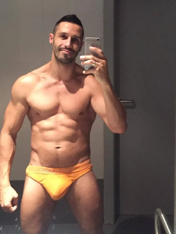 Homme torse nu en slip orange prenant un selfie dans un miroir de salle de bain