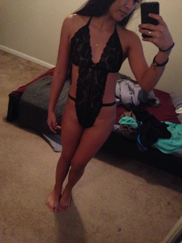 Femme en body noir en dentelle prenant un selfie devant un miroir dans une chambre.