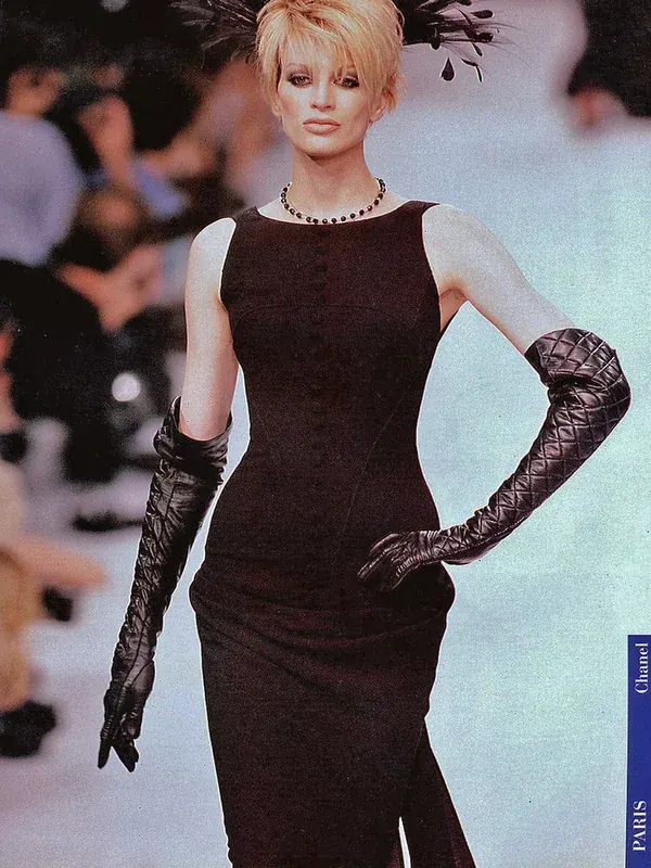 Mannequin aux cheveux blonds courts portant une robe noire et des gants longs lors d'un défilé Chanel à Paris.