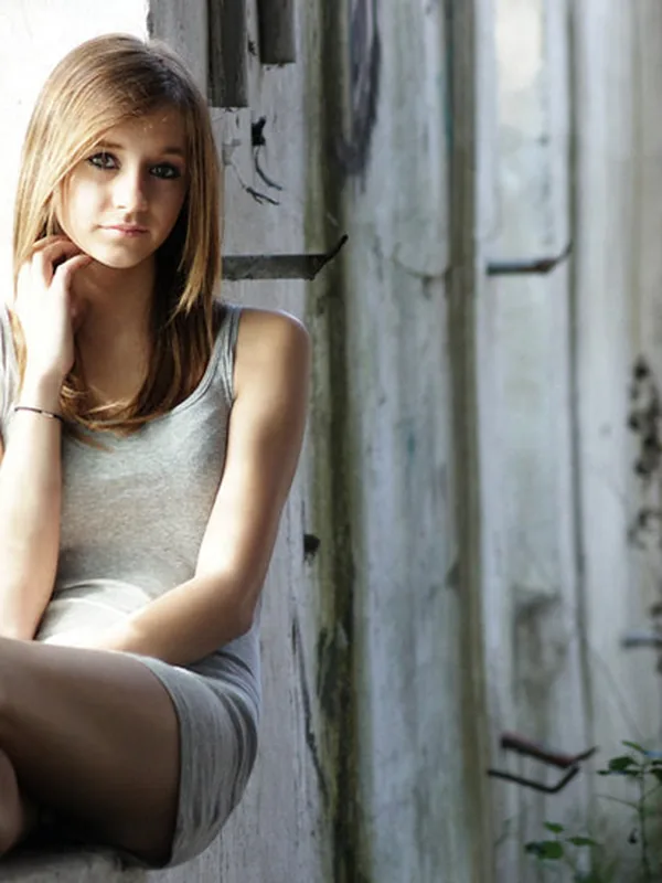Jeune femme aux cheveux bruns assise entre des poutres en bois, regardant l'objectif dans un cadre naturel.