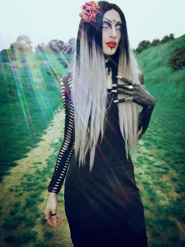 Personne en tenue gothique avec maquillage intense et fleur dans les cheveux, debout en extérieur.