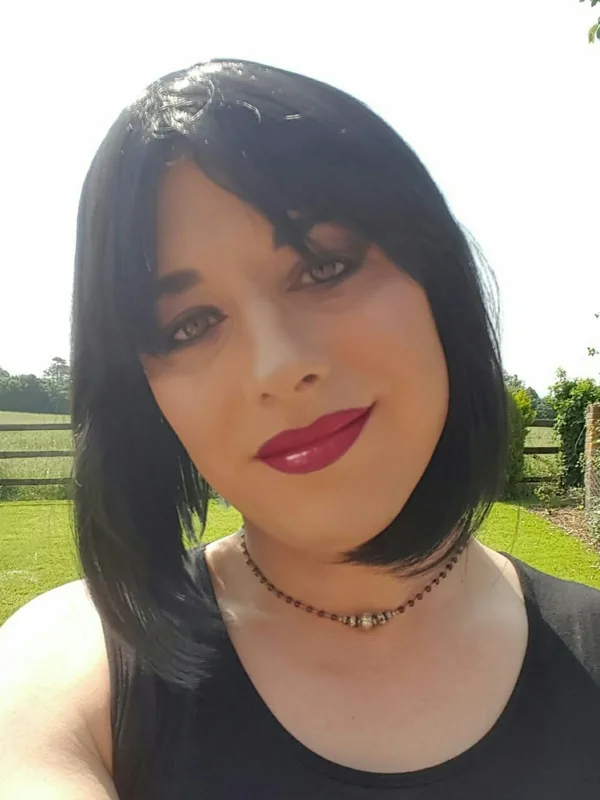 Portrait en extérieur d'une femme aux cheveux noirs portant un haut noir et un collier, souriant légèrement vers l'objectif.