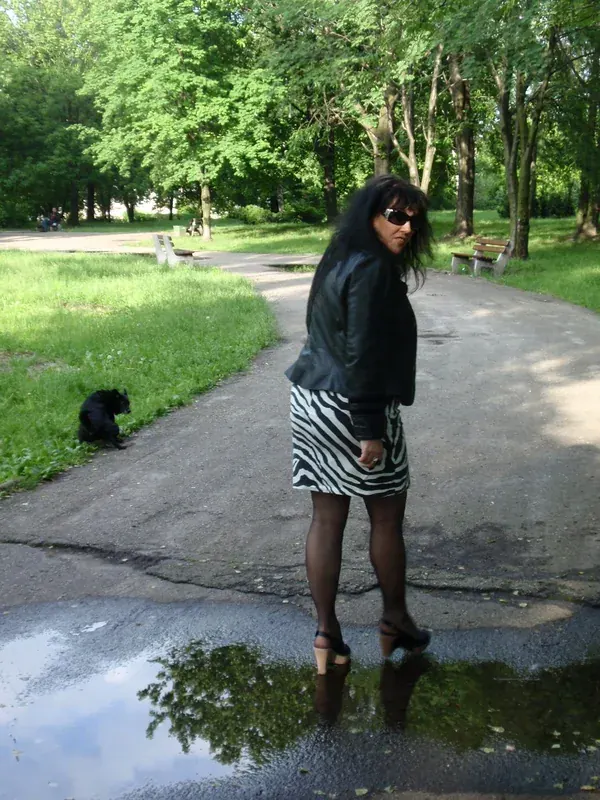 Femme en veste noire et jupe zèbre marchant dans un parc ensoleillé.
