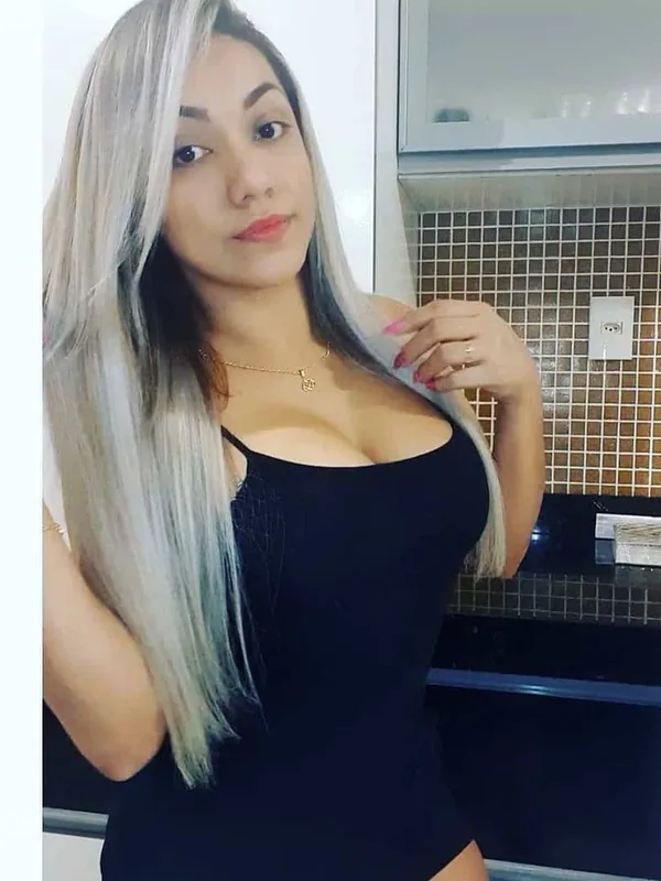 Portrait en buste d'une femme aux cheveux gris clair portant un haut noir, dans une cuisine.