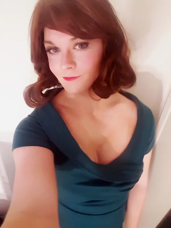 Portrait d'une femme aux cheveux bruns ondulés portant une robe verte foncée à décolleté plongeant, regardant l'objectif.