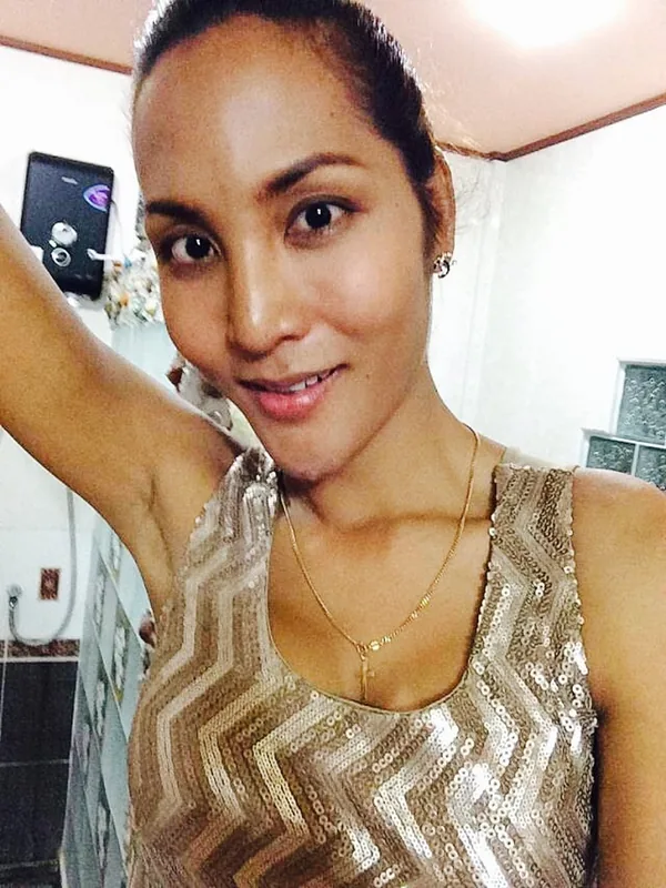 Portrait d'une femme souriante portant un haut à paillettes dorées, regardant l'objectif dans un intérieur éclairé.
