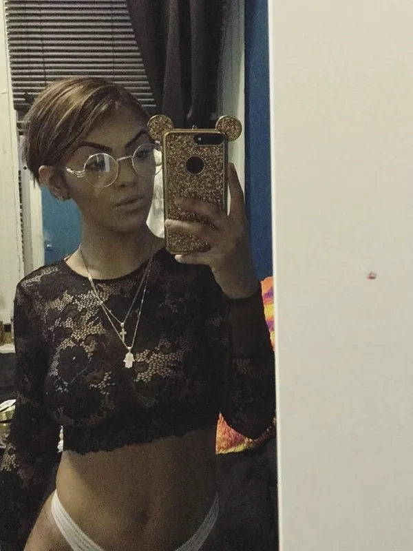 Portrait d'une femme prenant un selfie dans un miroir, portant des lunettes, un haut en dentelle noire et une culotte blanche.