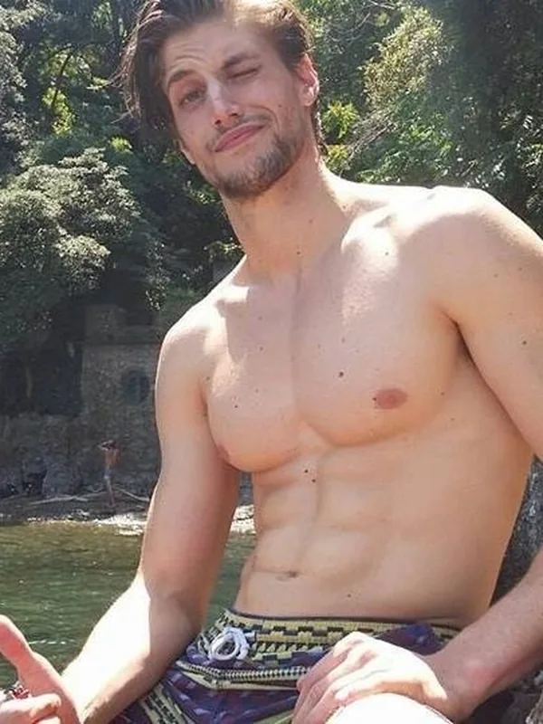 Un homme torse nu en maillot de bain assis sur un rocher près d'une rivière ensoleillée.