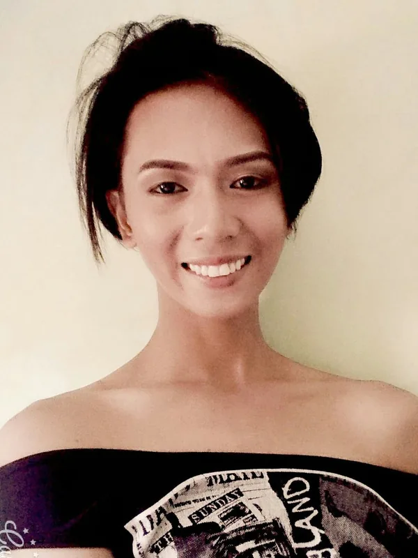 Portrait en buste d'une femme souriante, cheveux noirs courts, portant un haut noir décolleté, devant un fond clair.